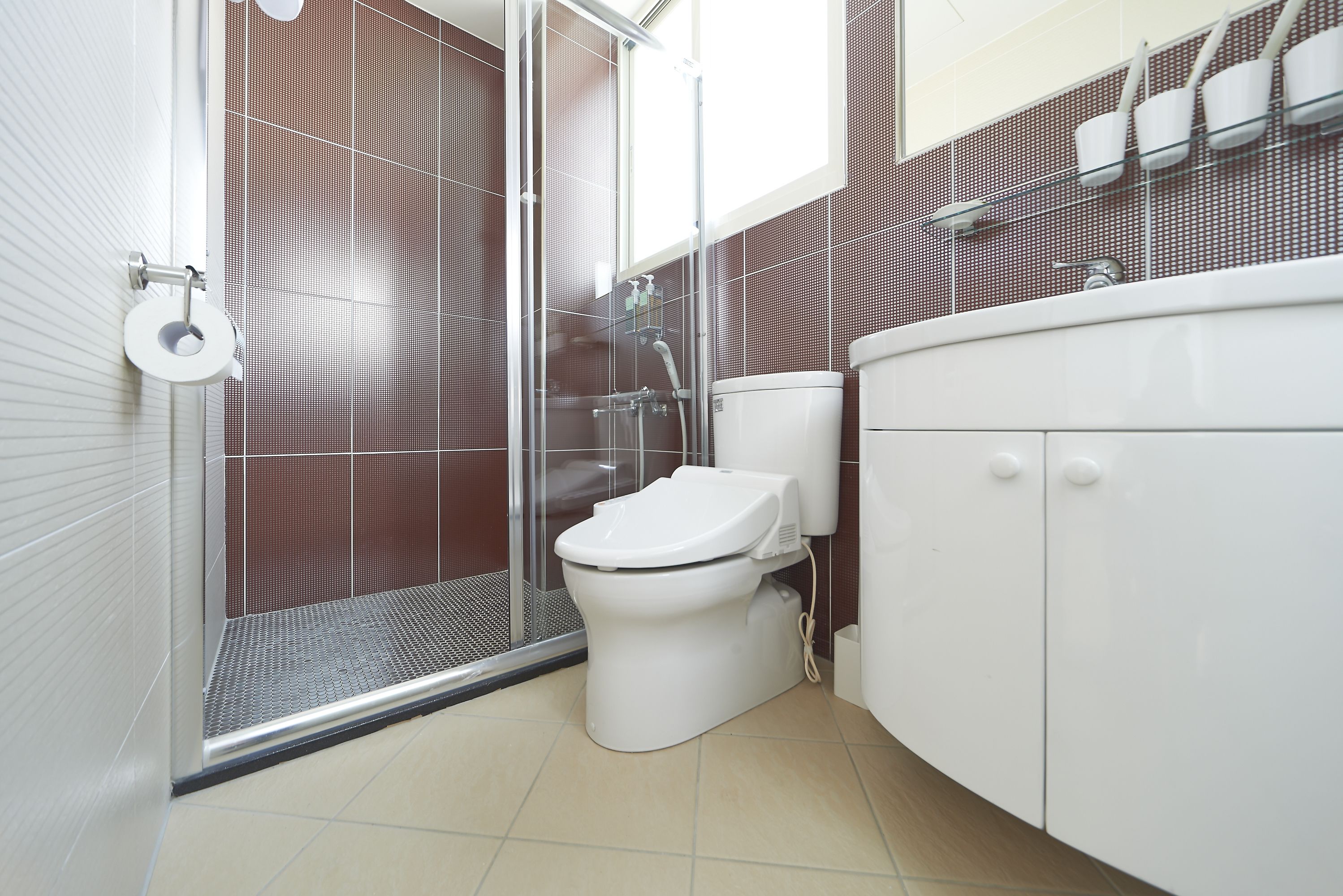 A modern bathroom with a glass shower enclosure, a white toilet, and a beige tiled floor.
