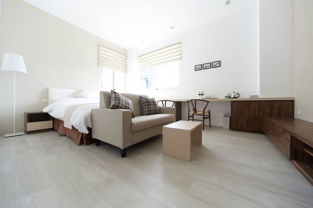 A modern hotel room with a bed, a sofa, a small table, a desk, and a chair.