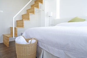 A bedroom with a wooden staircase, a bed with white bedding, a green pillow, and a wicker laundry basket. - Young Stay (Luodong)