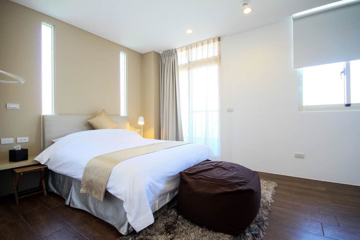 A bedroom with a bed, bedside table, lamp, and a window with curtains.
