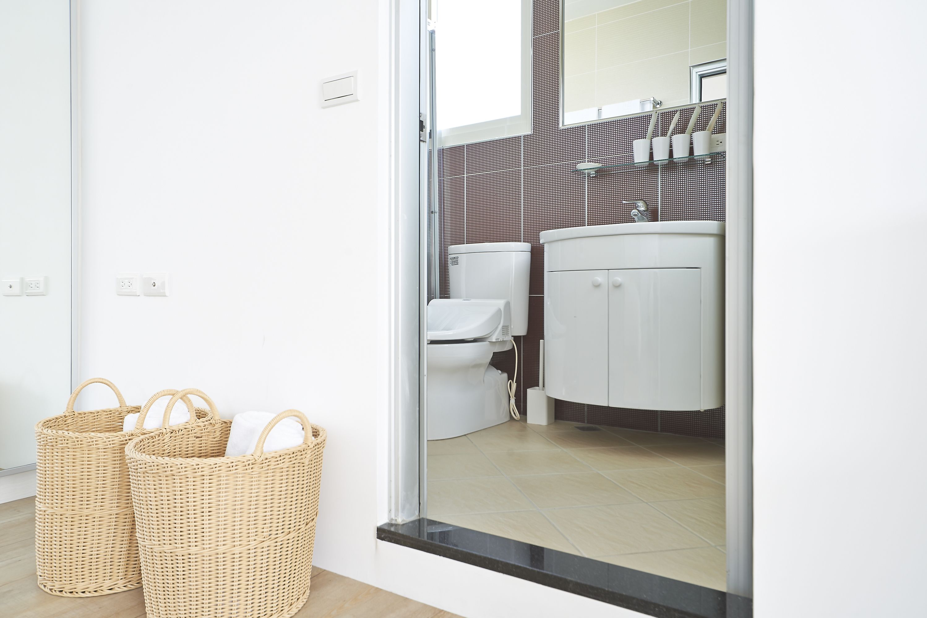 Une salle de bain moderne avec des toilettes, un lavabo et un miroir. On y trouve deux paniers en osier remplis de serviettes.