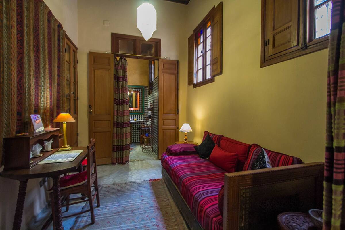Una habitación acogedora con una cama de madera, un escritorio con una lámpara y una alfombra estampada.