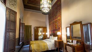 A traditional room with a checkered floor, a bed with a patterned bedspread, a wooden desk with a mirror, and a decorative wall hanging. - Riad Dar Cordoba (Fes)