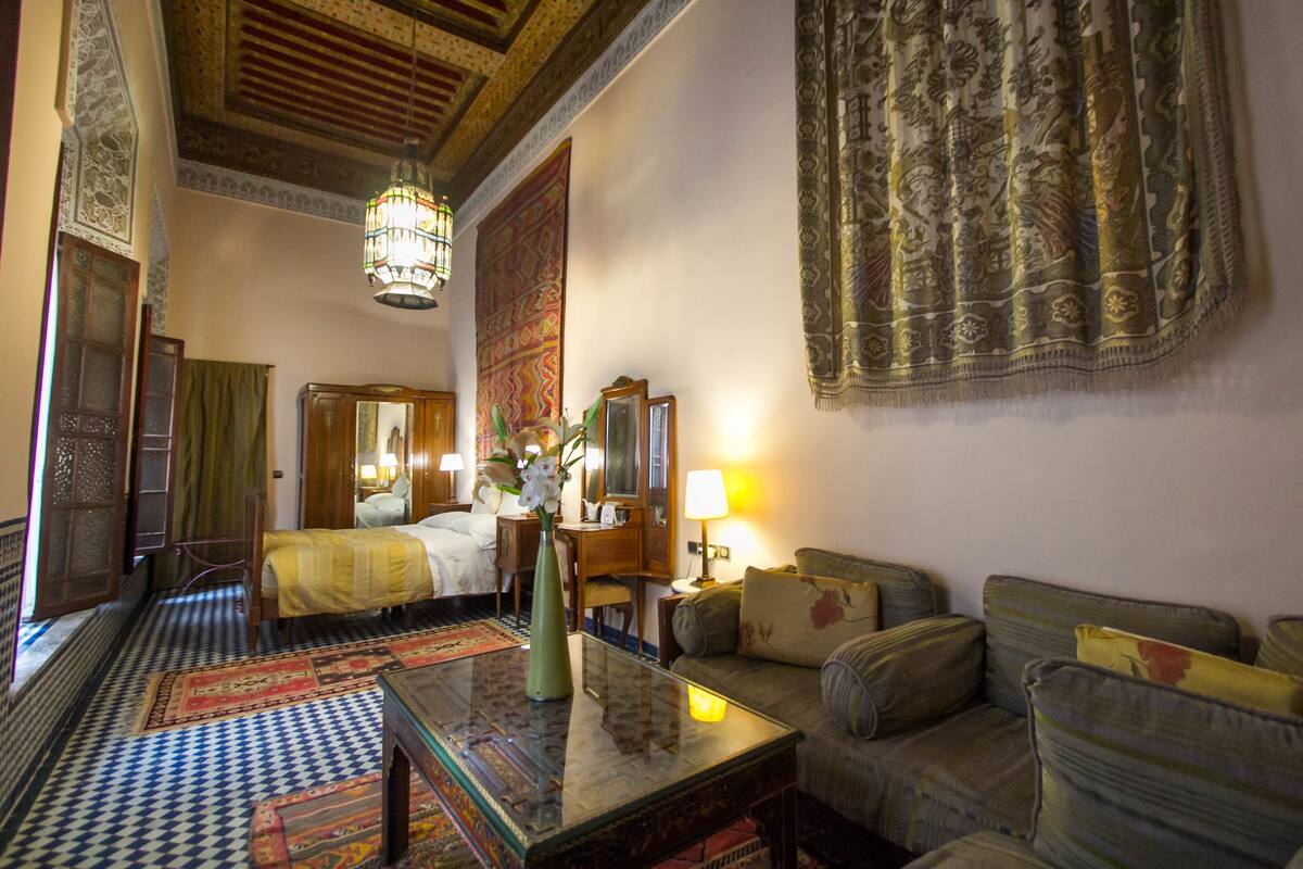Una habitación tradicional con cama, sofá, mesa y un tapiz colgado.
