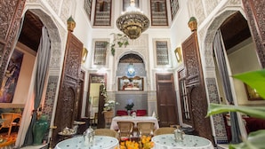 An ornate interior with high ceilings, intricate woodwork, and a central chandelier. Tables are set for dining, and there are potted plants adding greenery. - Riad Dar Cordoba (Fes)