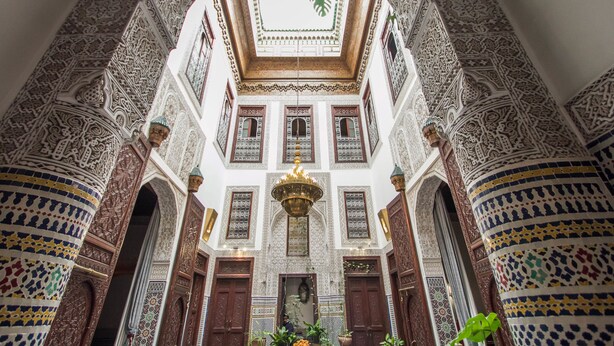 An ornate interior with intricate tile work, wooden doors, and a central chandelier. - Riad Dar Cordoba (Fes)