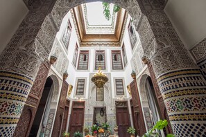 Um interior ornamentado com trabalhos em azulejos detalhados, portas de madeira e um candelabro central.