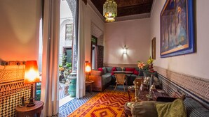 A cozy living room with a patterned rug, a sofa, a table with decorative items, and a hanging light fixture. - Riad Dar Cordoba (Fes)