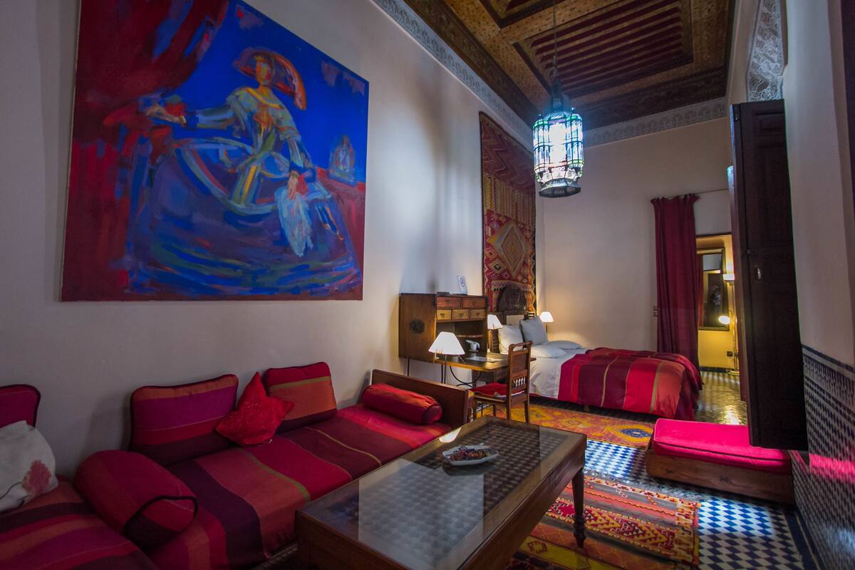 Una habitación con sofá, cama, mesa y un cuadro grande en la pared.