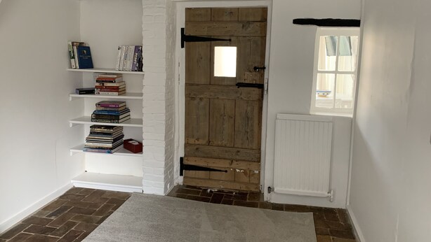 A room with a white brick wall, a wooden door, a white radiator, and a window. - Bell Cottage (Bury St Edmunds)