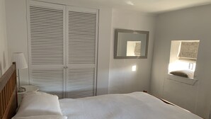 A bedroom with a bed, a nightstand, a lamp, a wardrobe, a mirror, and a window with a view. - Bell Cottage (Bury St Edmunds)
