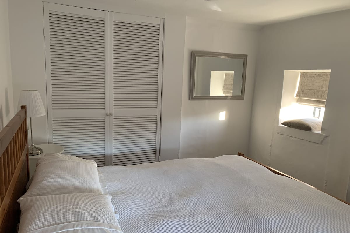 Een slaapkamer met een bed, nachtkastje, lamp, kledingkast, spiegel en een raam met uitzicht.