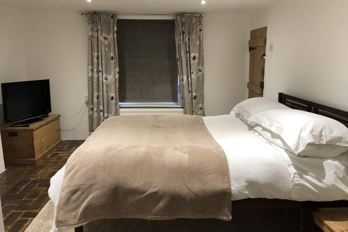 Een slaapkamer met een bed, een televisie op een houten dressoir en een raam met gordijnen.