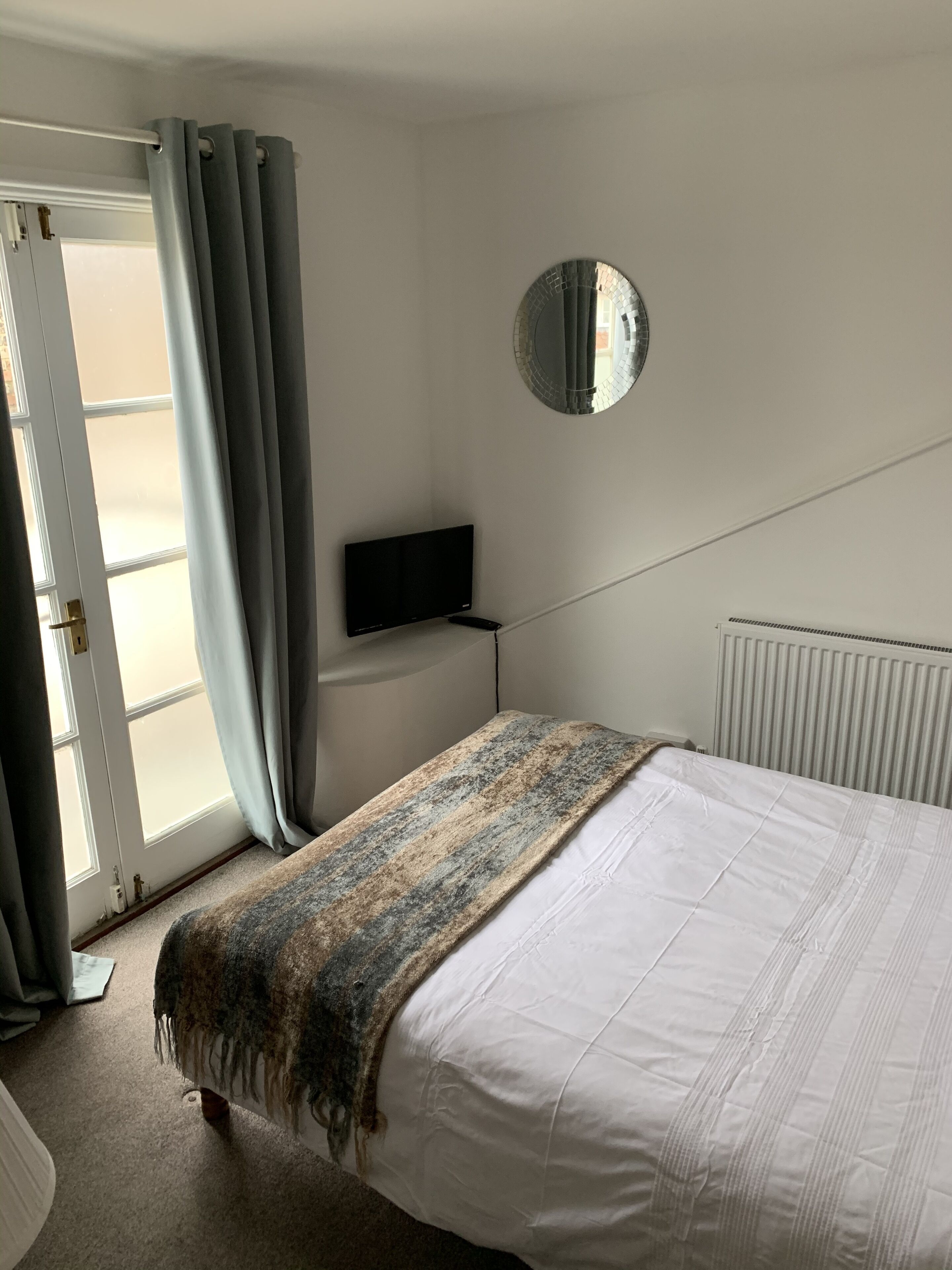 Un dormitorio con cama, televisor, espejo y puerta con cortinas.