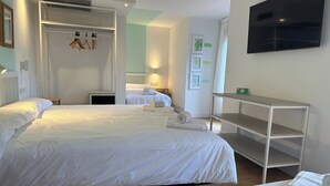 Habitación de hotel con dos camas, un televisor, un estante y una puerta que da a otra habitación.