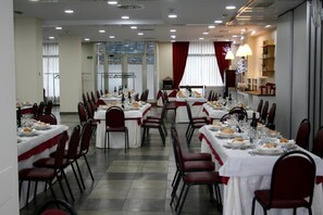 Ein formeller Speisesaal mit mehreren gedeckten Tischen, roten Stühlen und einem großen Fenster mit Vorhängen.