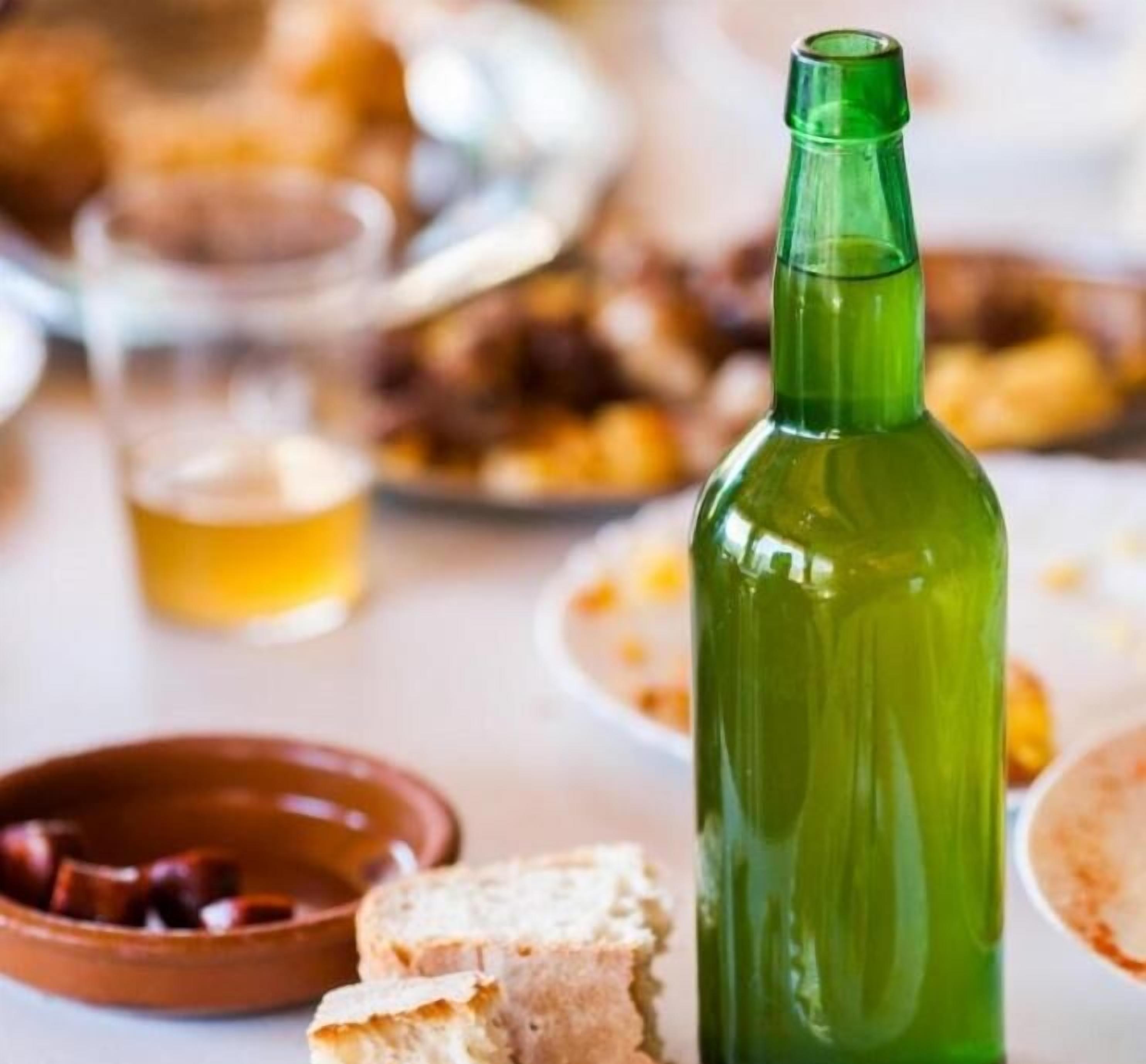 A table with a green bottle, a glass of yellow liquid, and various dishes including bread and olives.