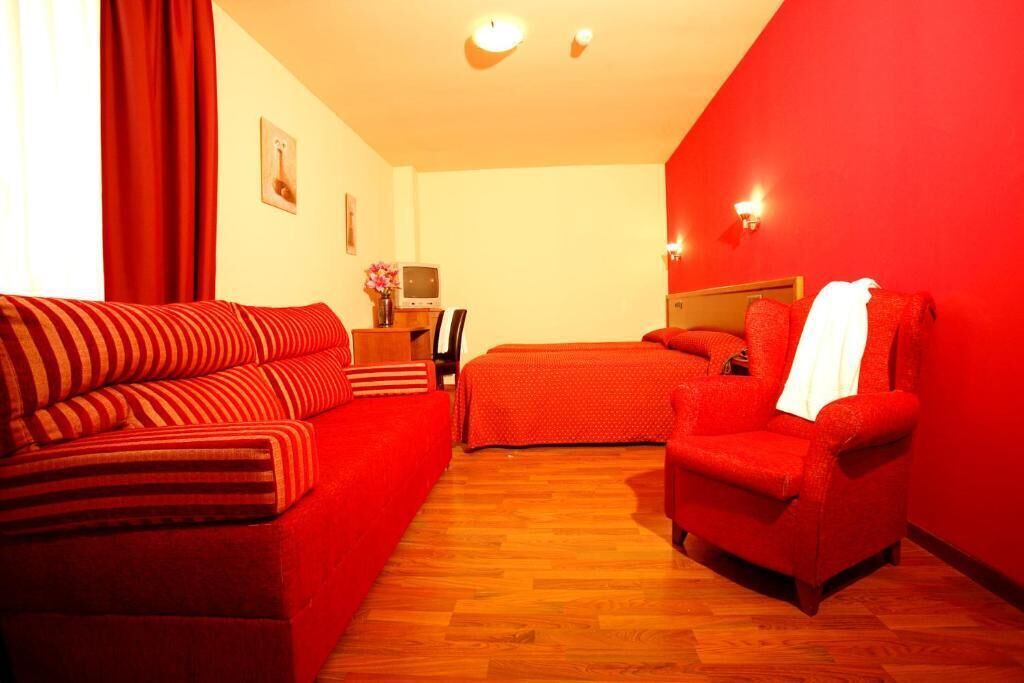 Camera d'albergo con un divano rosso, una poltrona rossa, un letto e un tavolino con un vaso di fiori.
