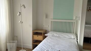 A hotel room with a neatly made bed, a bedside table, a floor lamp, and a small storage unit.