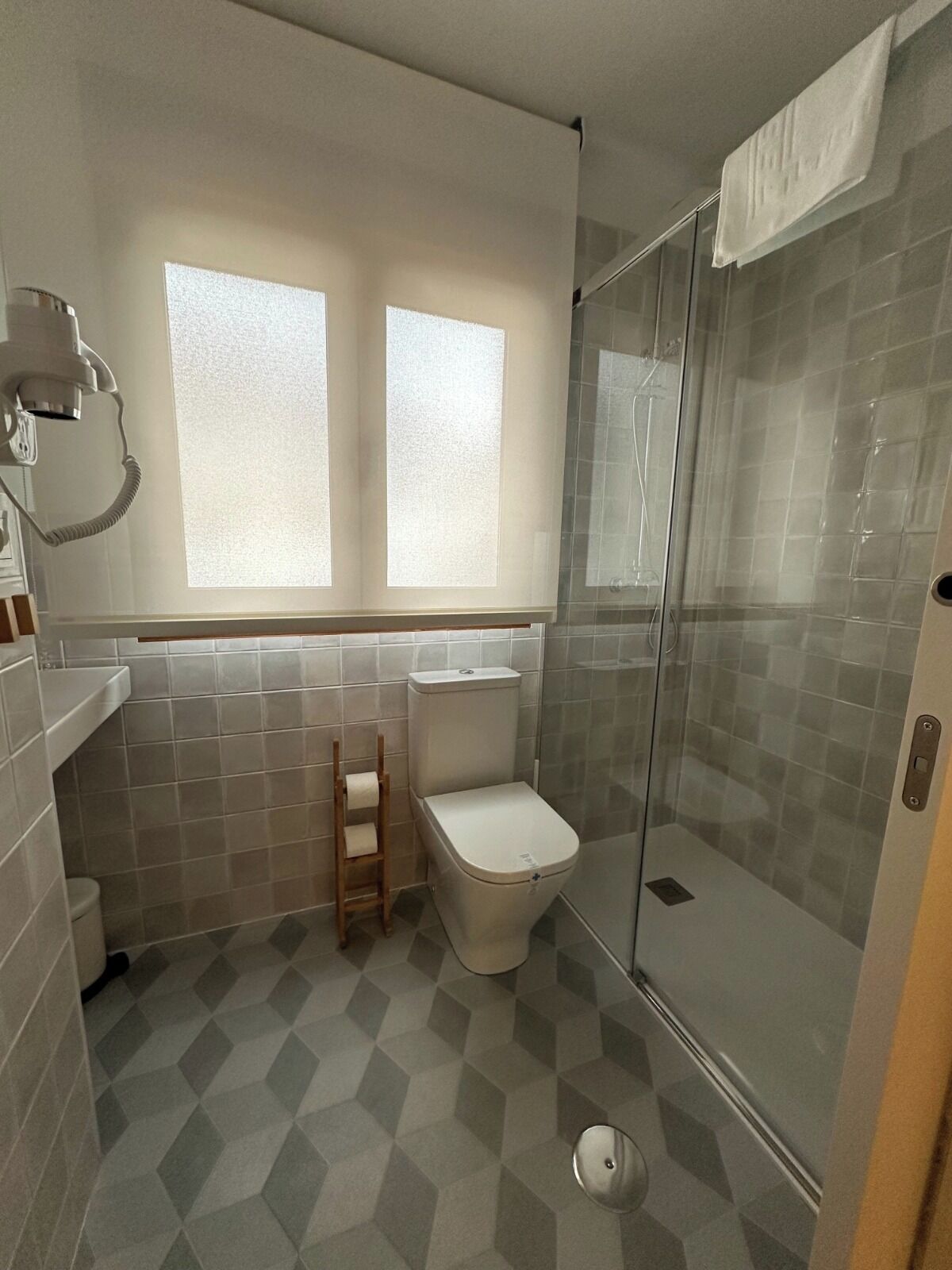 Un baño con inodoro, ducha con puerta de cristal y ventana sobre el inodoro.