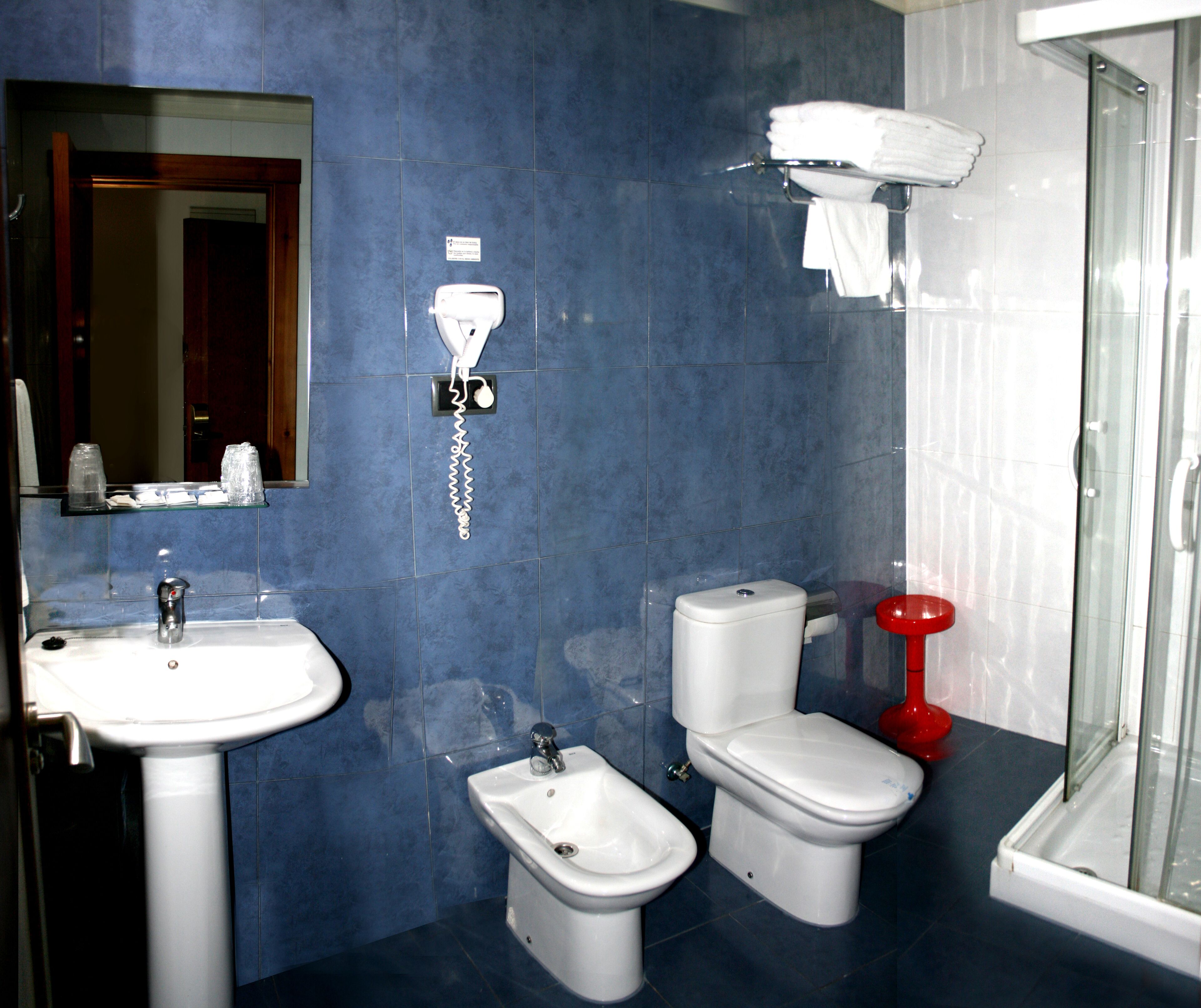 Baño con lavamanos, bidé, inodoro y cabina de ducha de vidrio.