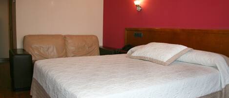 A neatly made bed with a white quilt, a wooden headboard, and a red wall with a wall-mounted light.