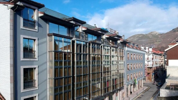 Un hotel moderno con amplios ventanales, techo plano y vistas a la calle y las montañas.