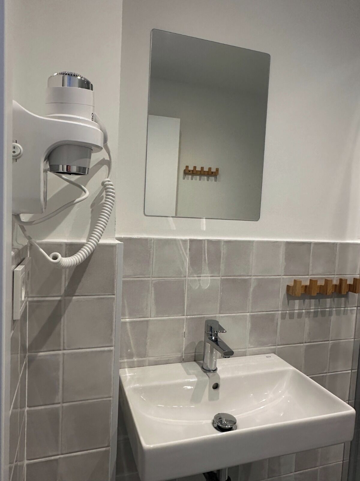 A bathroom with a white sink, a mirror, and a hairdryer mounted on the wall.