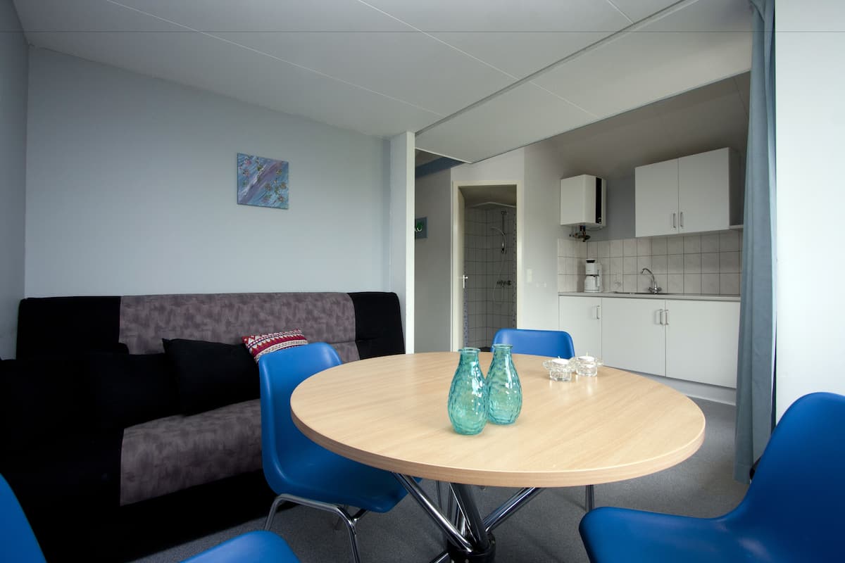 Ein modernes Wohnzimmer mit einem runden Tisch, blauen Stühlen, einer Couch und einer Küche im Hintergrund.