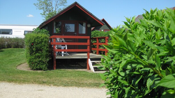Eine Hütte mit Veranda, überdachter Sitzgelegenheit und einem Schotterweg.