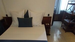 A neatly made bed with white and blue bedding, a dark green pillow, and a wooden headboard. - Aviavy Plage Hôtel (Nosy Be)