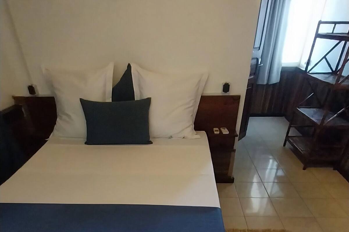 A neatly made bed with white and blue bedding, a dark green pillow, and a wooden headboard.