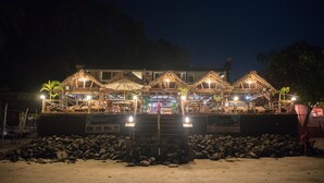 A beachfront resort with thatched-roof structures, a sandy beach, and a rocky foreground. - Aviavy Plage Hôtel (Nosy Be)