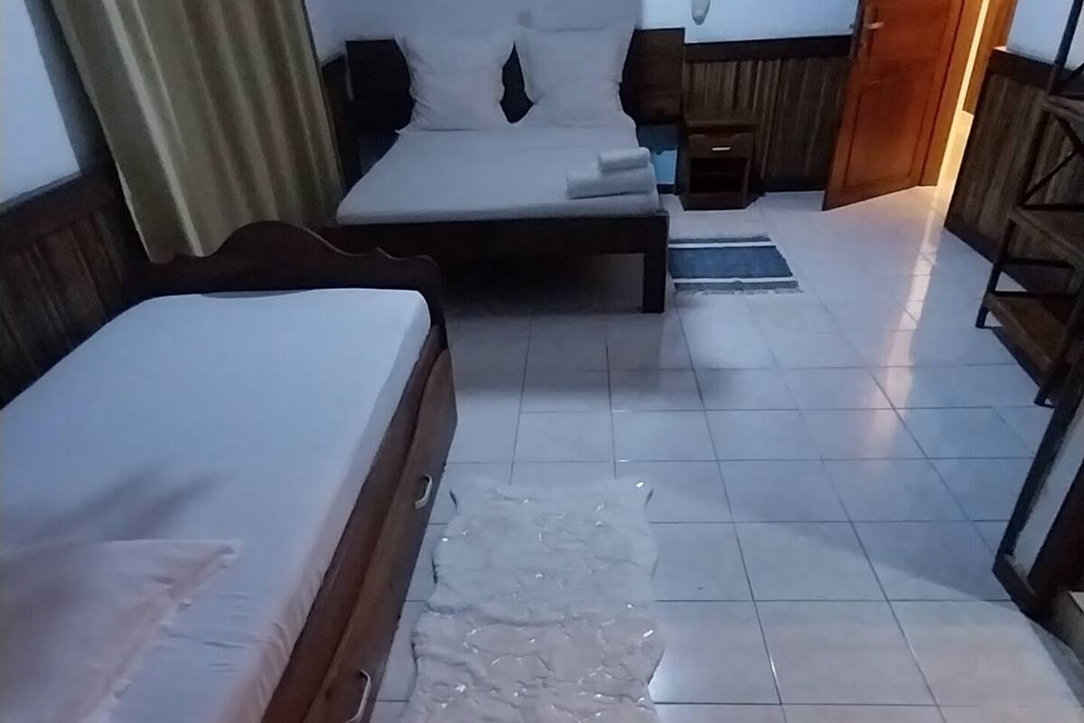 A hotel room with a bed, a small table, a chair, and a wooden wardrobe.