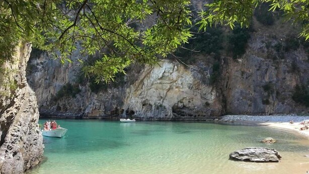 A beach with clear turquoise water, rocky cliffs, and a boat in the distance. - B&B Donna Maja (Centola)