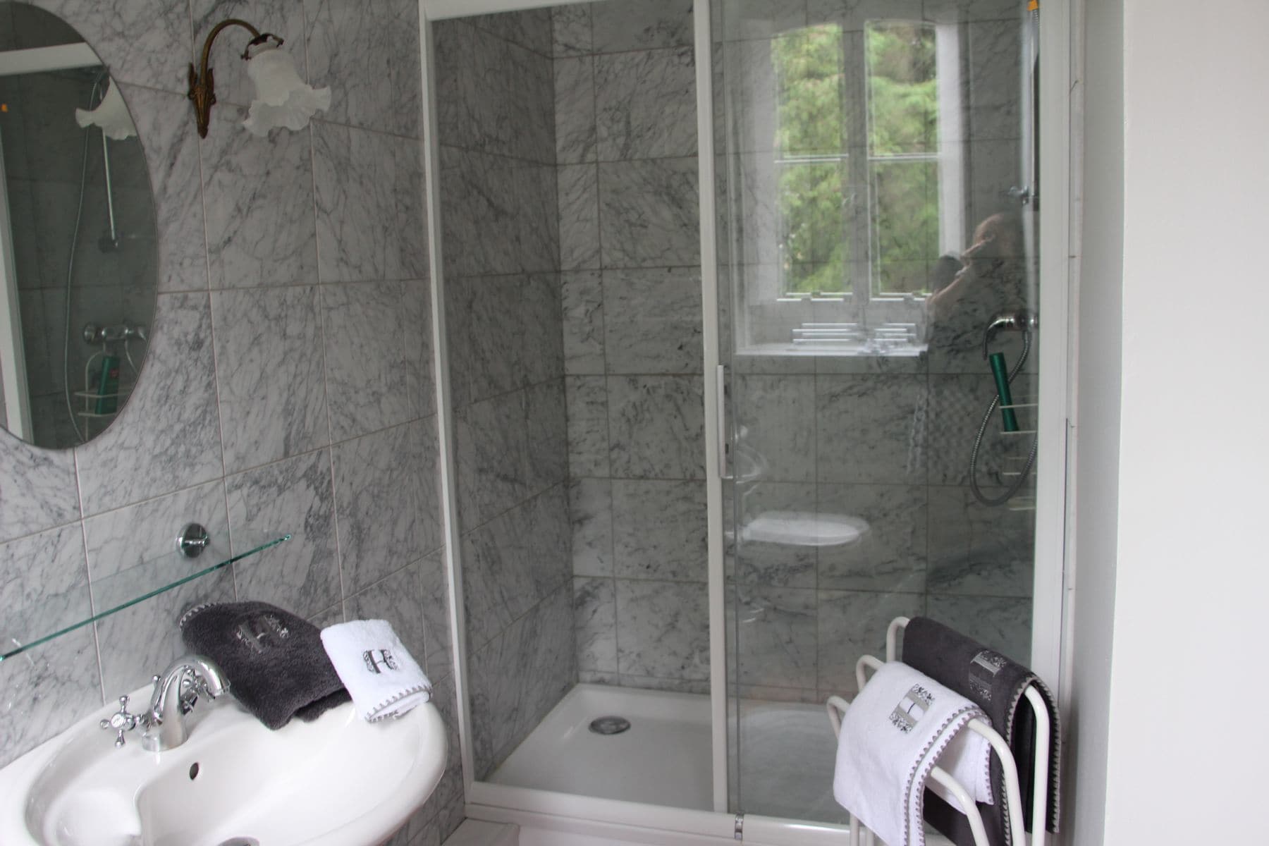 Ein Badezimmer mit Duschkabine, Waschbecken mit Spiegel und zwei Handtüchern an der Wand.