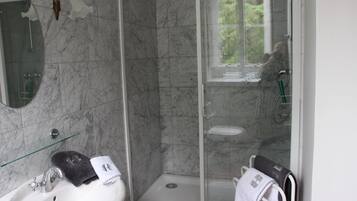 Een badkamer met een douche in glazen cabine, een wastafel met spiegel en twee handdoeken aan de wand.