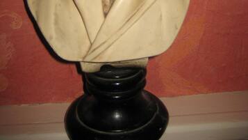 Una escultura de busto sobre un pedestal negro frente a una pared roja con diseño.