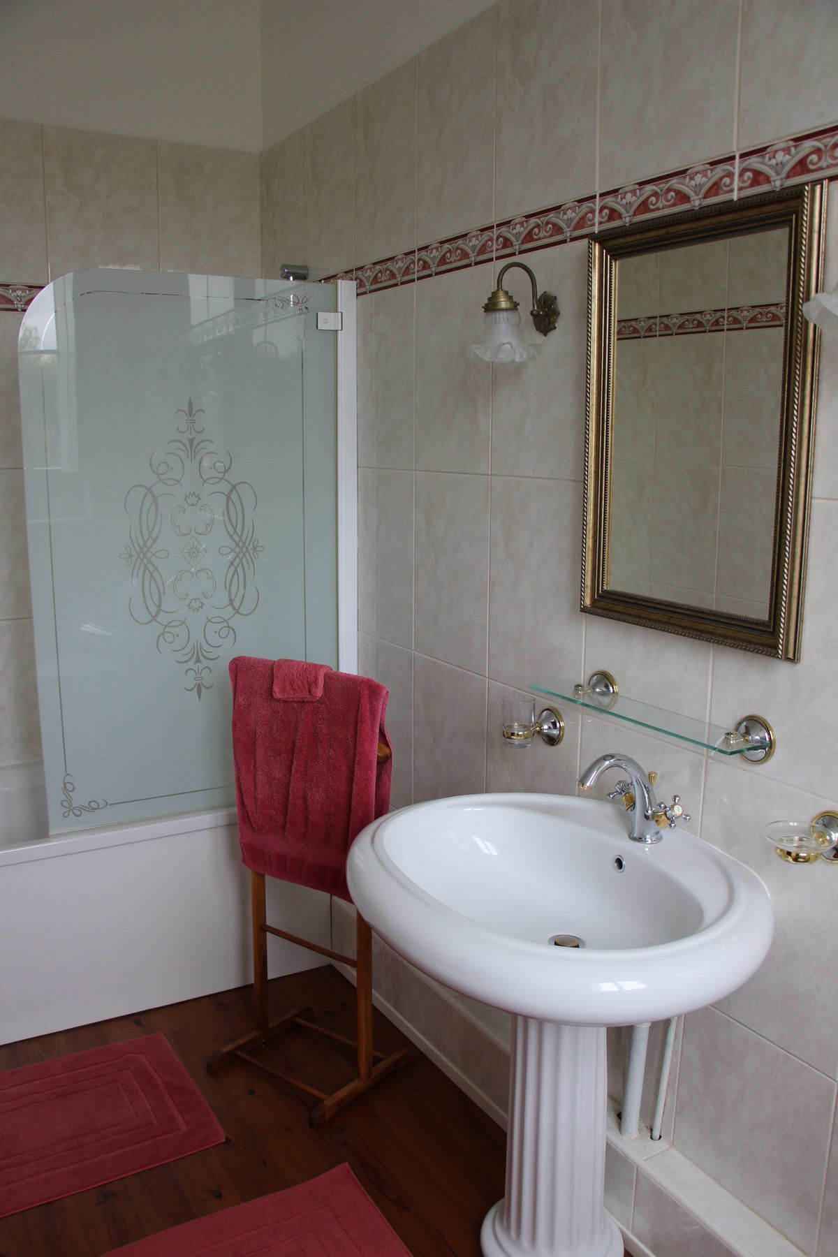 A bathroom with a glass shower enclosure, a white sink with a gold faucet, and a mirror with a decorative frame.