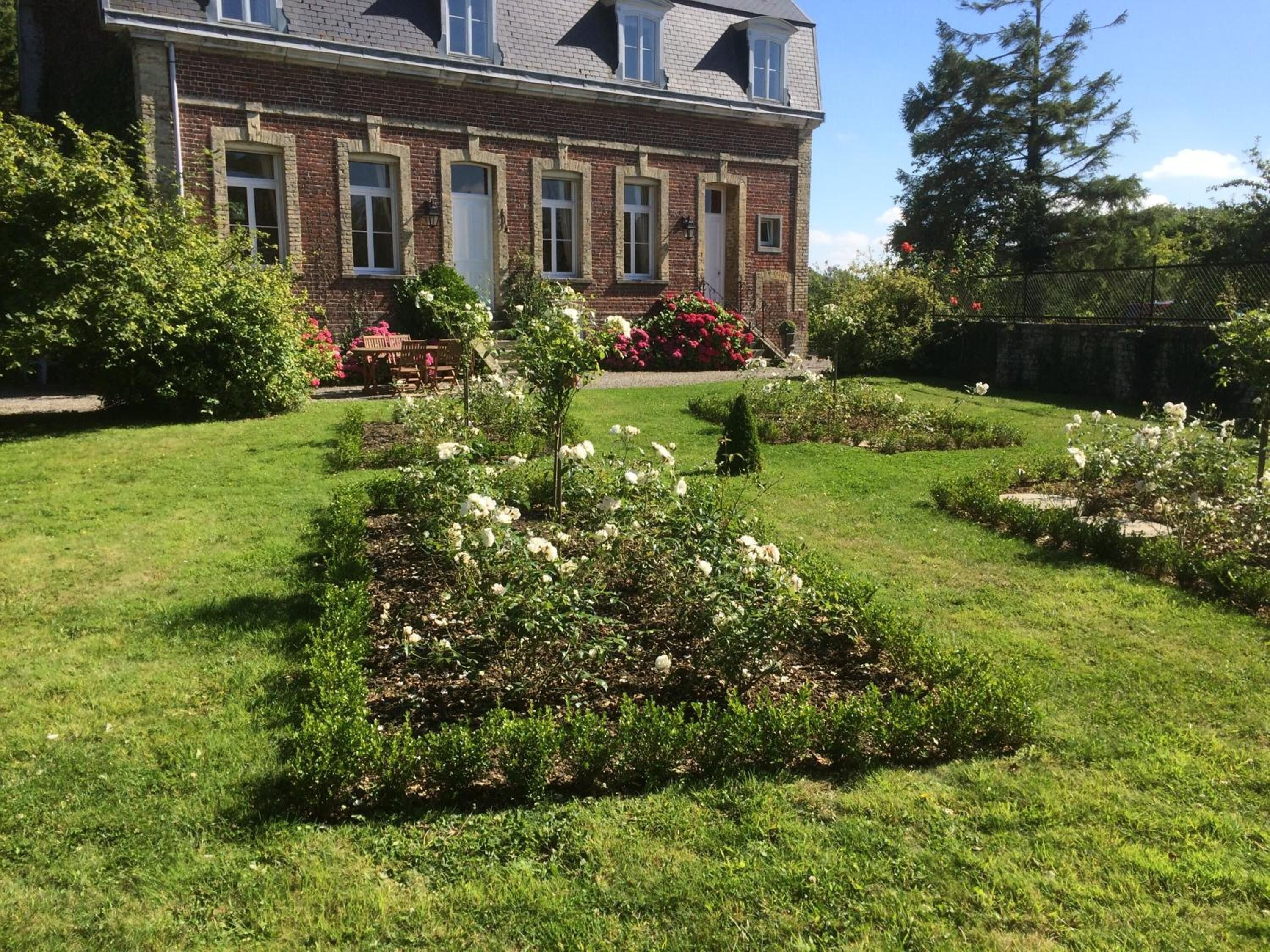 Une maison en briques avec un jardin bien entretenu, agrémenté de rosiers blancs et de divers arbustes.