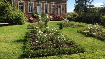 Une maison en briques avec un jardin bien entretenu, agrémenté de rosiers blancs et de divers arbustes.
