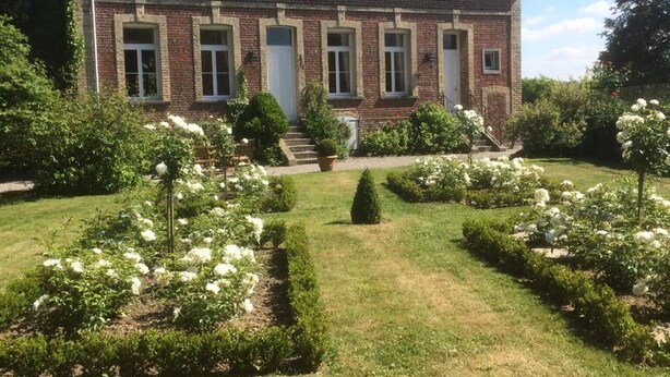 A large, two-story brick house with a symmetrical facade, multiple windows, and a well-maintained garden with white flowers and hedges. - Le Clos Boutenelle (Eperlecques)