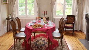 A dining room with a round table covered by a red tablecloth, surrounded by wooden chairs. - Le Clos Boutenelle (Eperlecques)