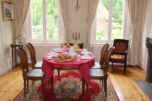 Uma sala de jantar com uma mesa redonda coberta por toalha vermelha, rodeada por cadeiras de madeira.