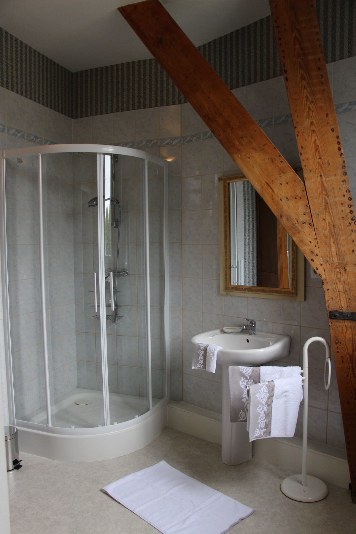 Un baño con ducha de vidrio, lavamanos con toalla y estructura de vigas de madera.