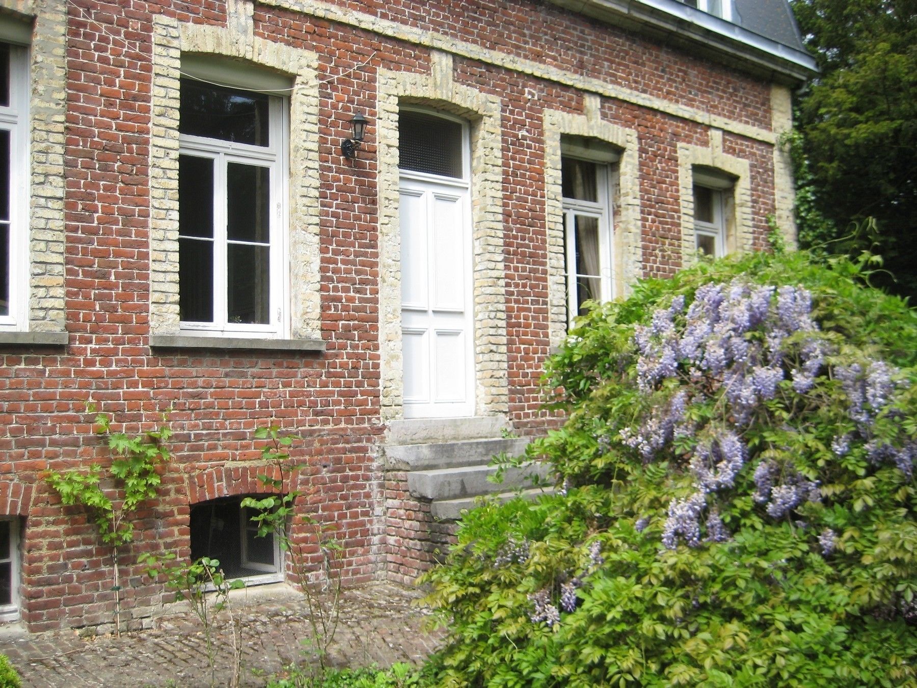 A brick building with three white-framed windows and a small door.