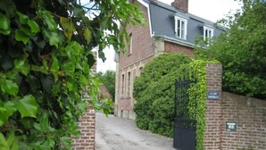 A gravel driveway leading to a brick building with a black gate and a sign that reads "La Cure Montrose." - Le Clos Boutenelle (Eperlecques)