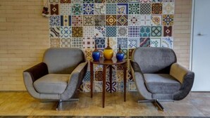 Una habitación con dos sillones grises, una pequeña mesa de madera con dos jarrones y una pared de azulejos coloridos.