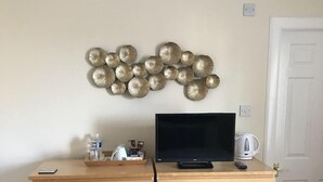 Une pièce comprenant une commode en bois, un téléviseur posé dessus, un objet décoratif fixé au mur et une porte.