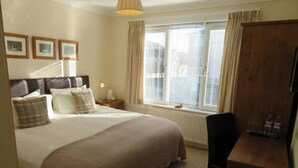 Une chambre d’hôtel avec un grand lit, un bureau, une chaise, une fenêtre avec des stores et un radiateur.